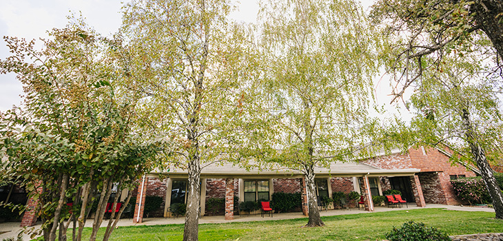 The community with brick walls and pilers with lush grass and mature trees in bloom out front.