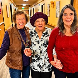 Three women holding hands in Oakwood Village hallway.