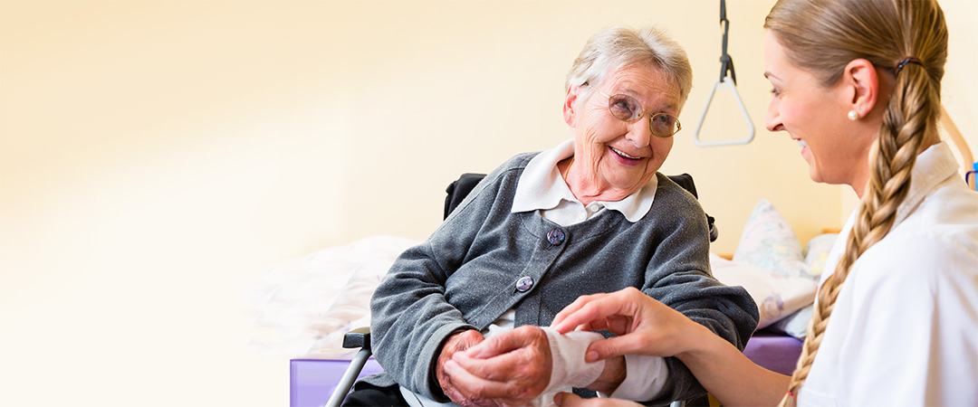 Healthcare worker with long blonde braid helping senior woman with wrap around her wrist.