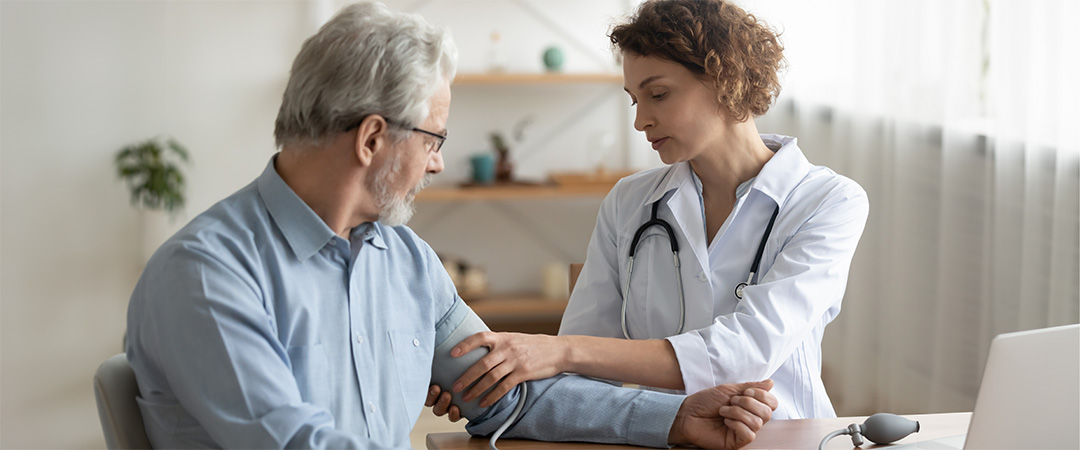 Doctor taking blood pressure of man in blue shirt.