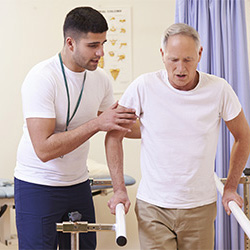 rehab therapist with a resident in the gym holding the handrails