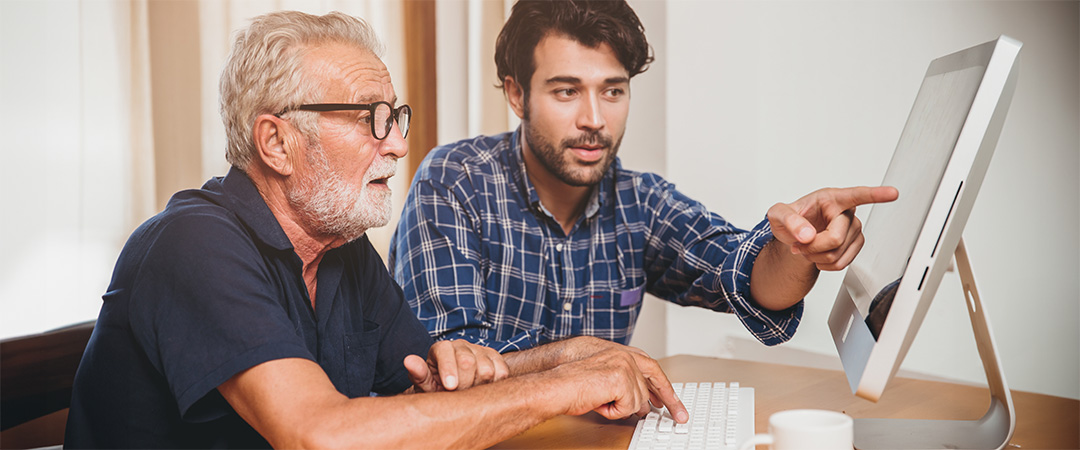 A young man helping an elderly man on a computer