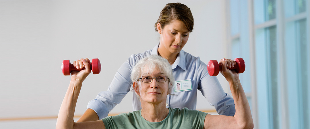 An elderly woman lifting weights with the help of a physical therapist