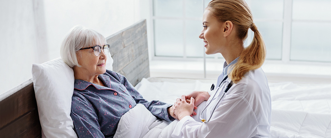 Elderly woman in hospital bed while doctor is holding her hand