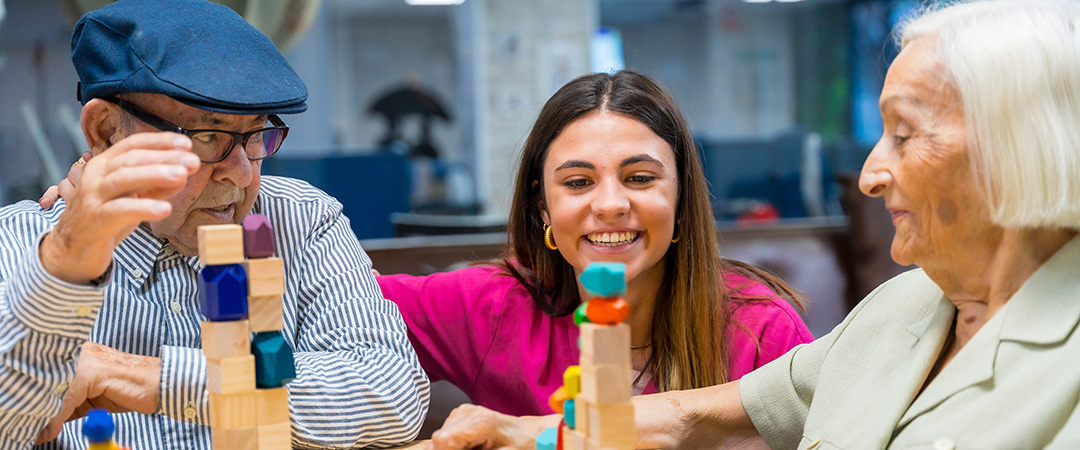 Caregiver watching two seniors play a block stacking game