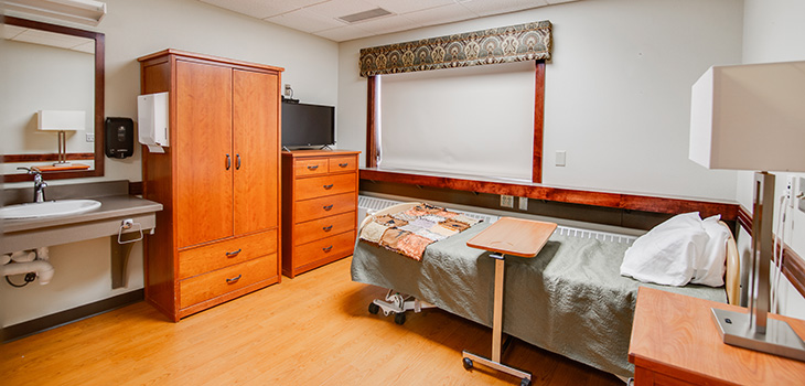 Private bedroom including single bed, bedside table, dresser, small TV, wide window, and personal sink.