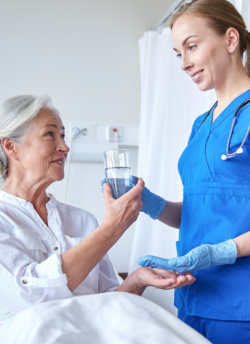 nurse helping a resident with her medication while sitting up in bed