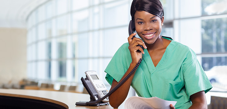A healthcare worker in mint green scrubs talking on the phone.